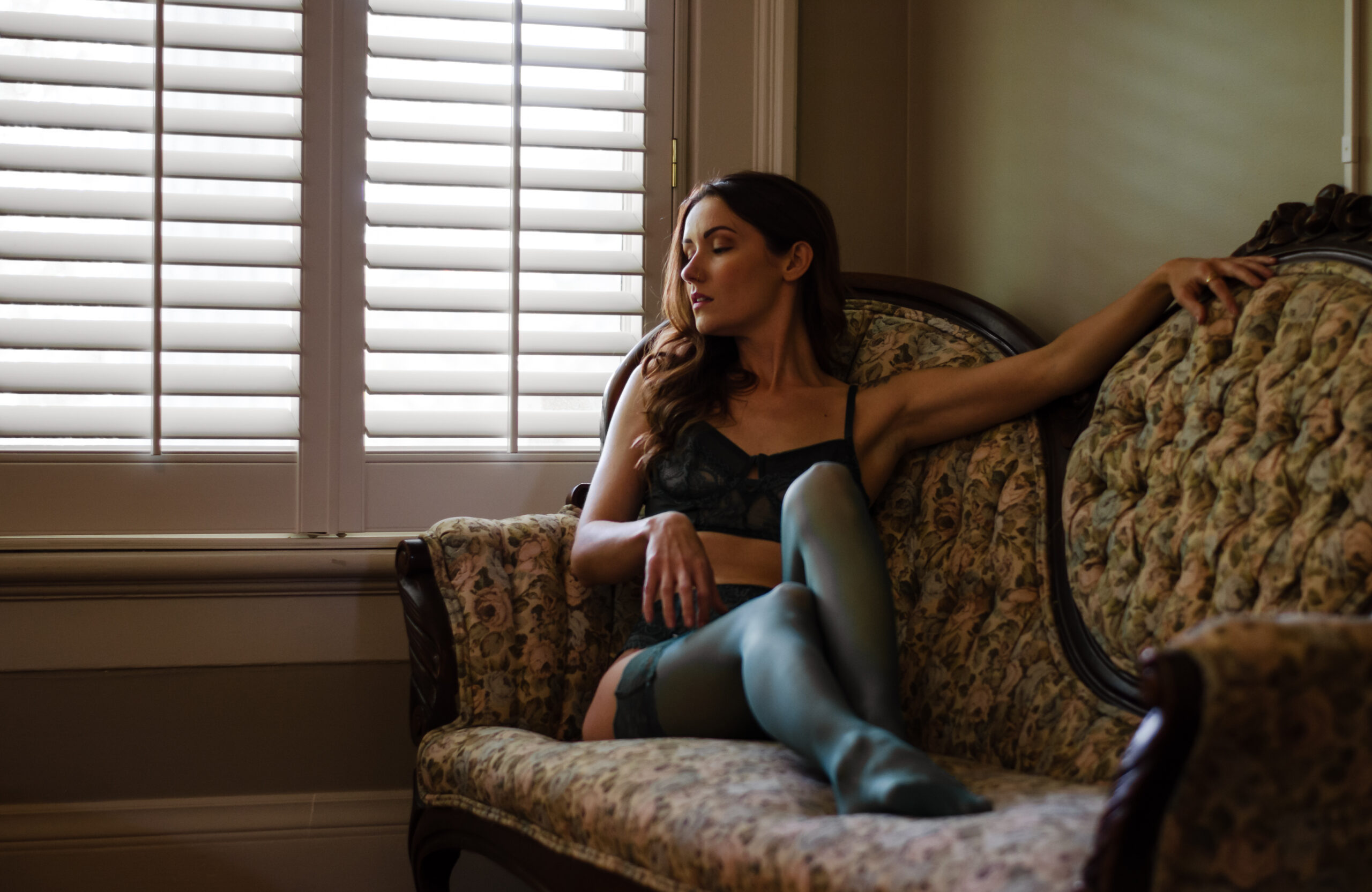 Women in green lingerie lounges on sofa and looks out window.